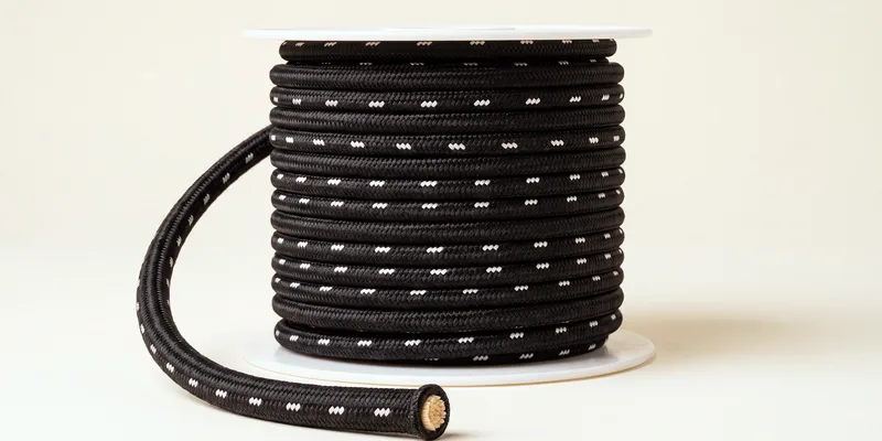 A spool of black bungee cord flecked with white, a length looping out in front with the cut end showing the pale rubber core inside the braided sheath