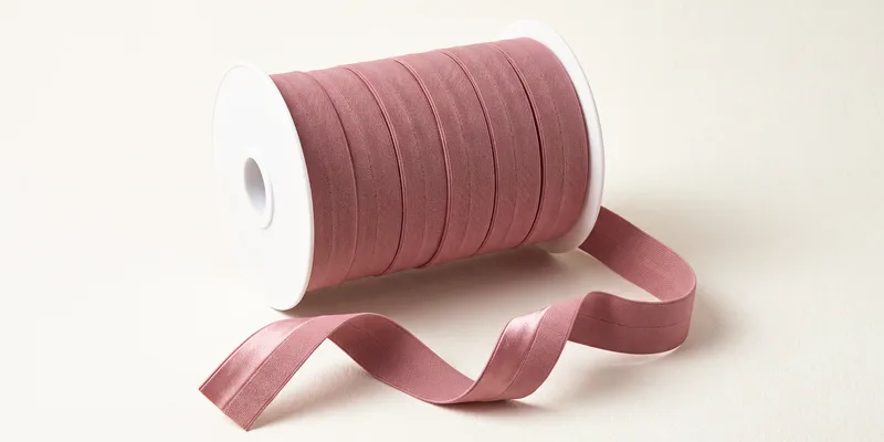 A spool of dusty rose fold over elastic with the tail unwound, showing the satin face and the matte reverse